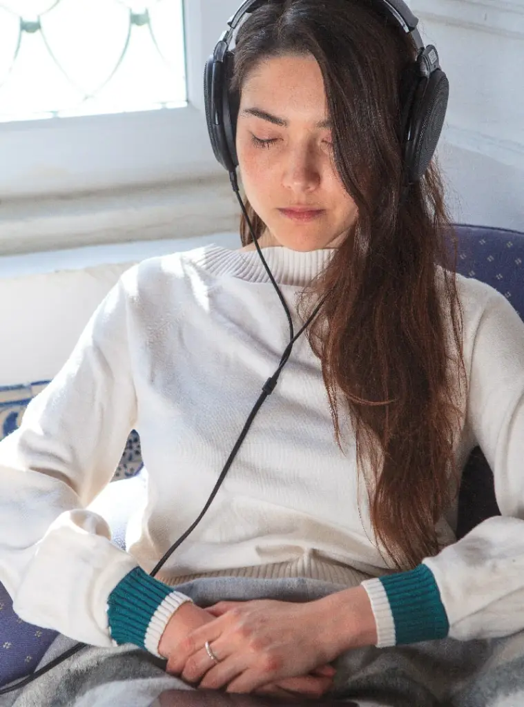 Woman sits with her eyes closed and hands together calmly listening to Wavepaths on headphones
