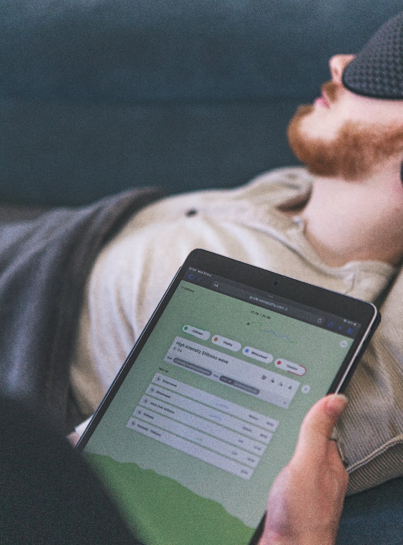 Therapists holds iPad display Wavepaths. In the background a Ketamine Therapy patient wears eye shades and headphones